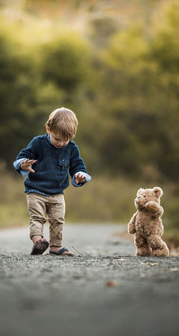 a young boy walking down a road next to a teddy bear