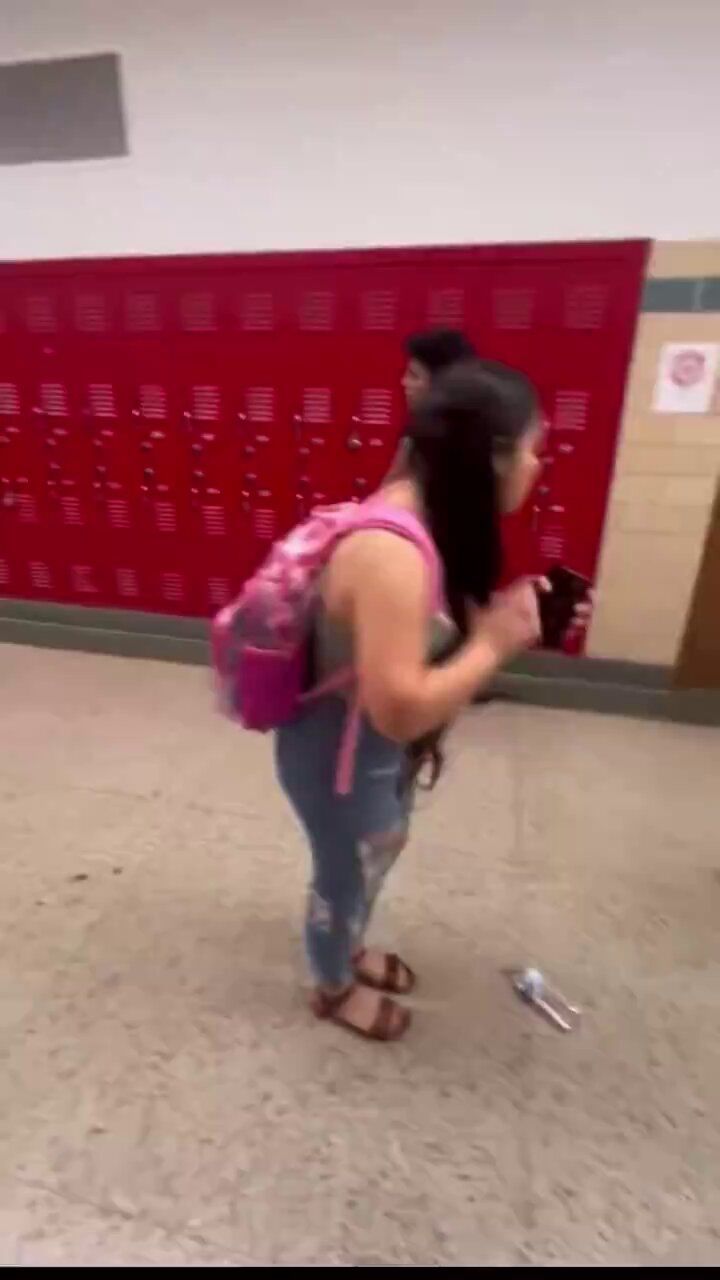 a woman with a pink backpack is looking at her cell phone in the middle of an empty hallway