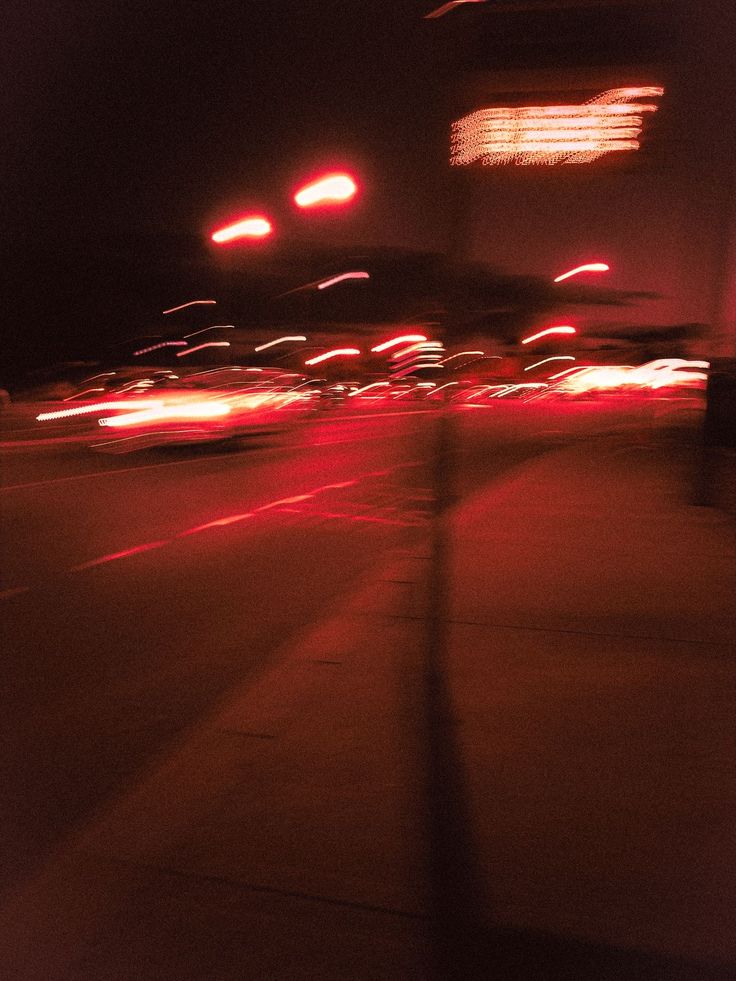 blurry photograph of city street at night with red lights and buildings in the background