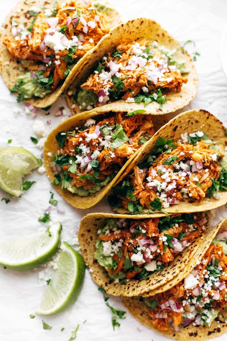 four tacos with shredded meat, cilantro and salsa on the side next to lime wedges