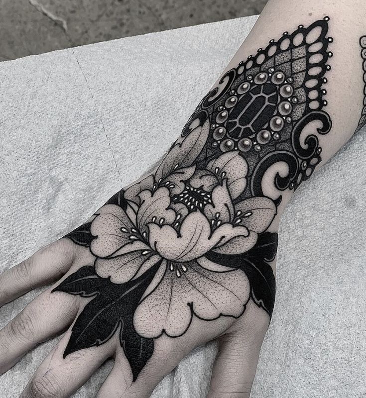 a woman's hand with a black and white flower tattoo on the left arm