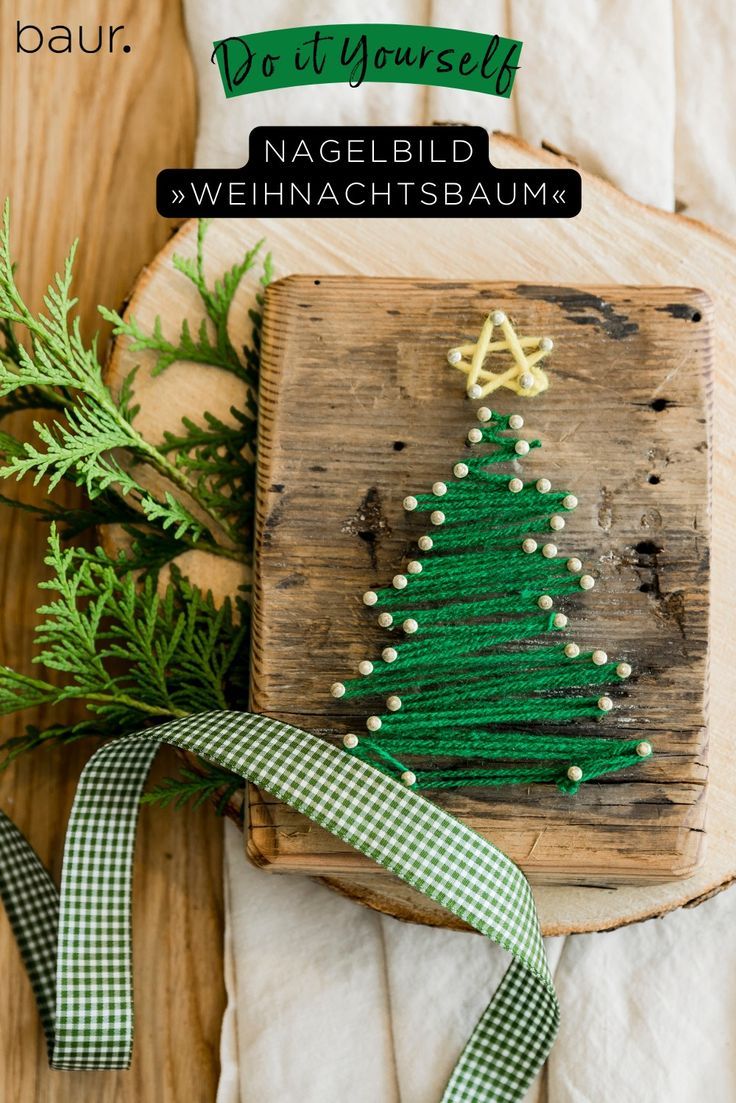 a green christmas tree on top of a wooden board next to some greenery and ribbon