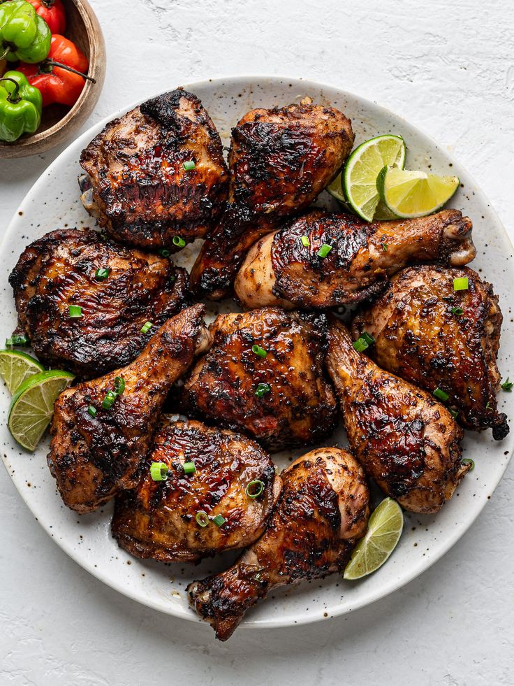 grilled chicken with limes and tomatoes on a white plate next to a bowl of peppers