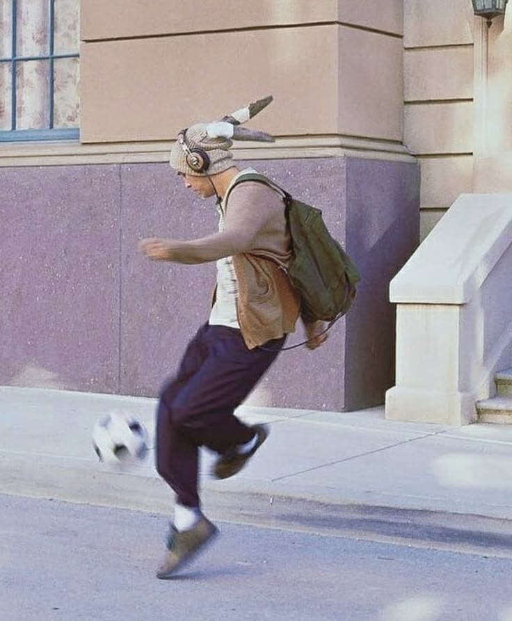 a man is kicking a soccer ball on the street while wearing headphones and a backpack