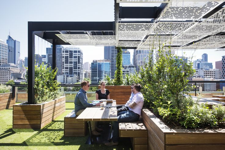 two people sitting at a table on top of a roof garden with city buildings in the background