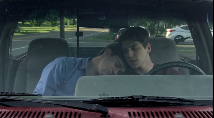 two people sitting in the driver's seat of a red car, one is kissing the other