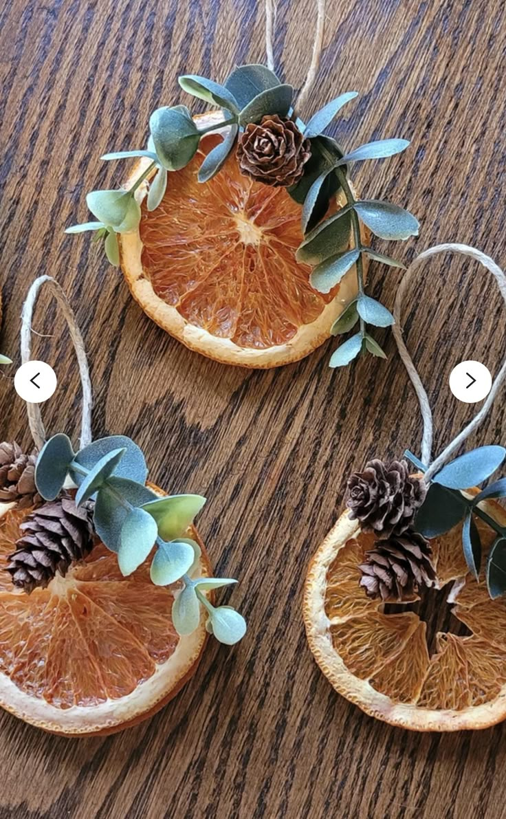 three orange slices with pine cones and leaves on them sitting on top of a wooden table