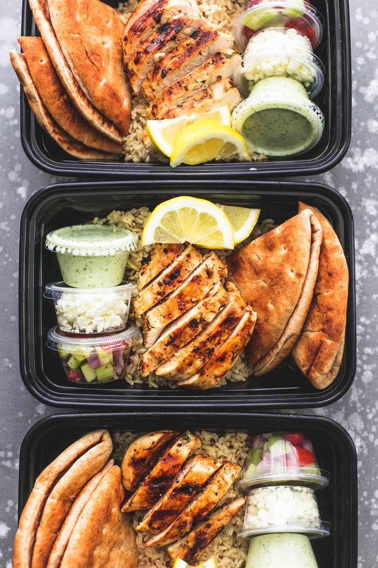 two trays filled with chicken, rice and lemon wedges next to each other