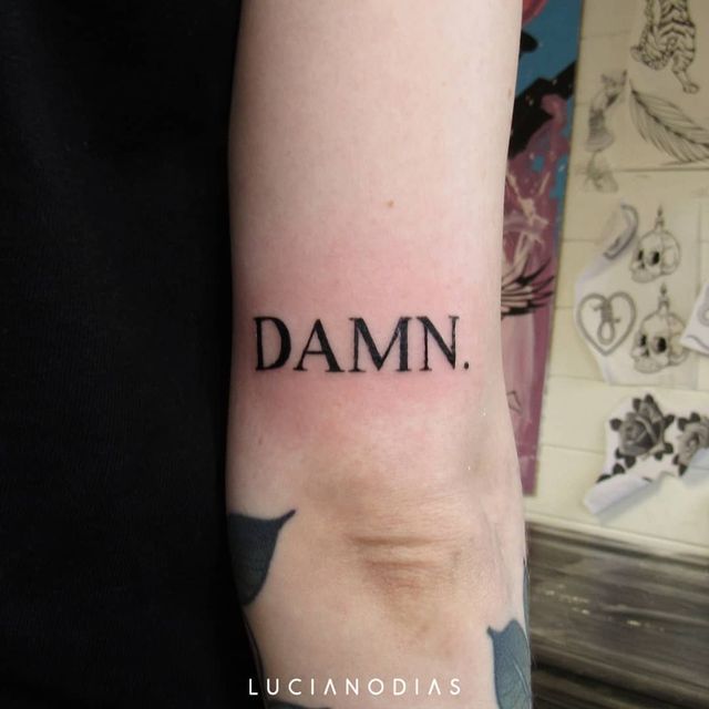 a person with a tattoo on their arm has the word damn written in black ink