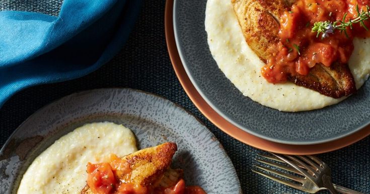 two plates topped with fish covered in marinara sauce next to some pita bread