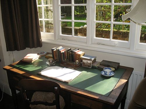 a table with books and a bowl on it in front of two windows that are open