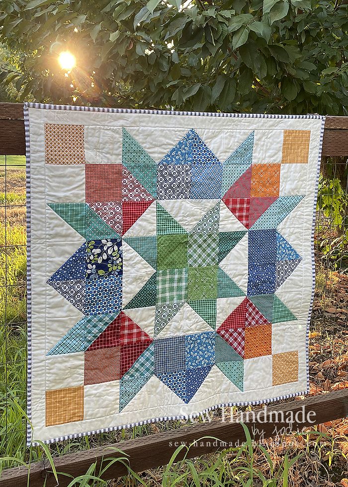 a quilt hanging on a fence with the sun shining in the background