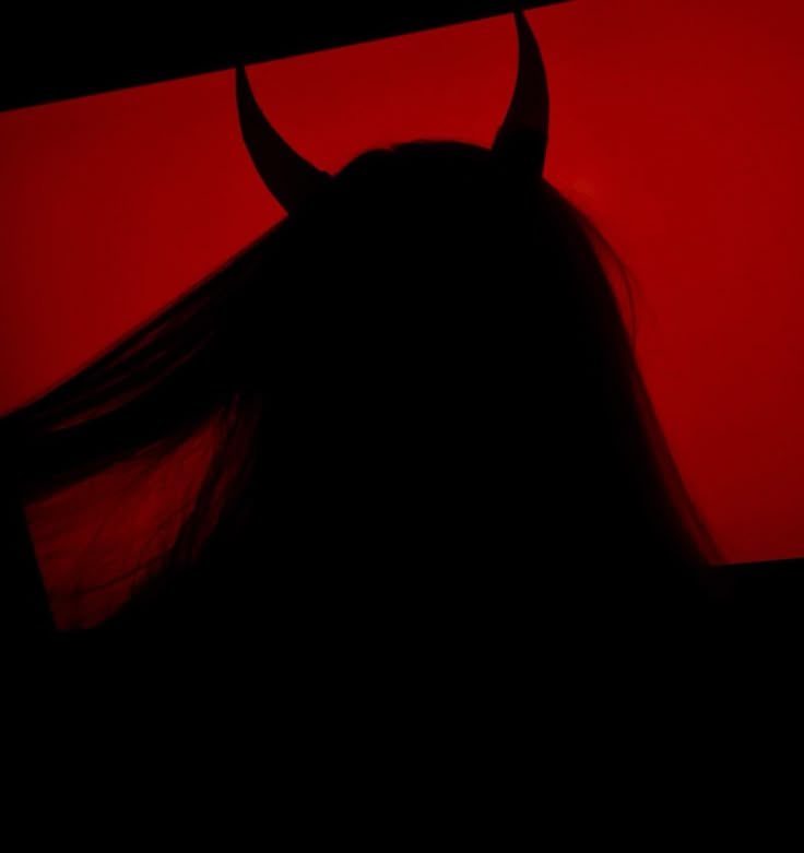 the silhouette of a woman with long hair and horns on her head, against a red background