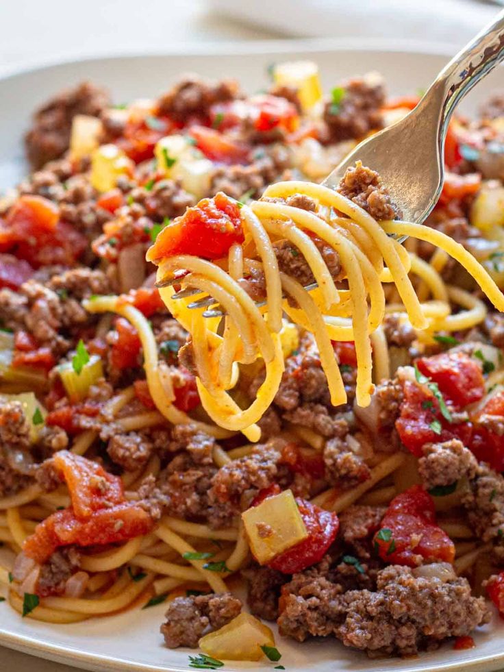 a fork full of spaghetti with meat and tomato sauce on the top is being lifted from a white plate