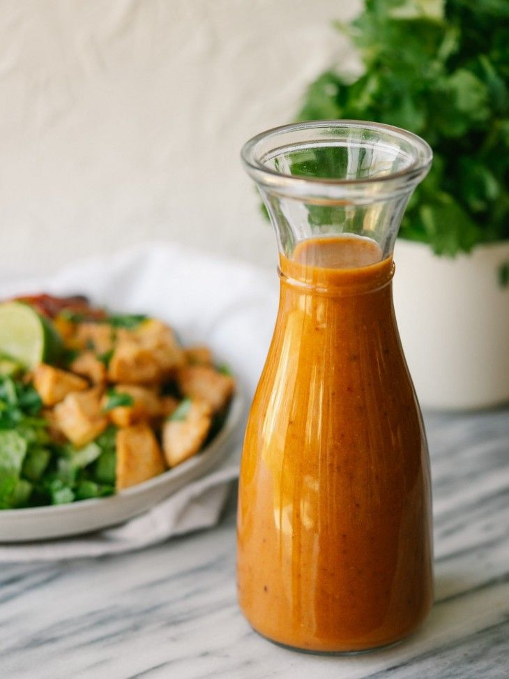 a glass bottle filled with dressing next to a bowl of salad on a marble table