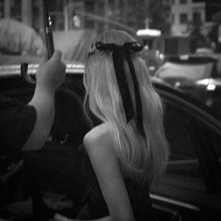 a woman with long blonde hair sitting in a car looking at her cell phone while holding an umbrella