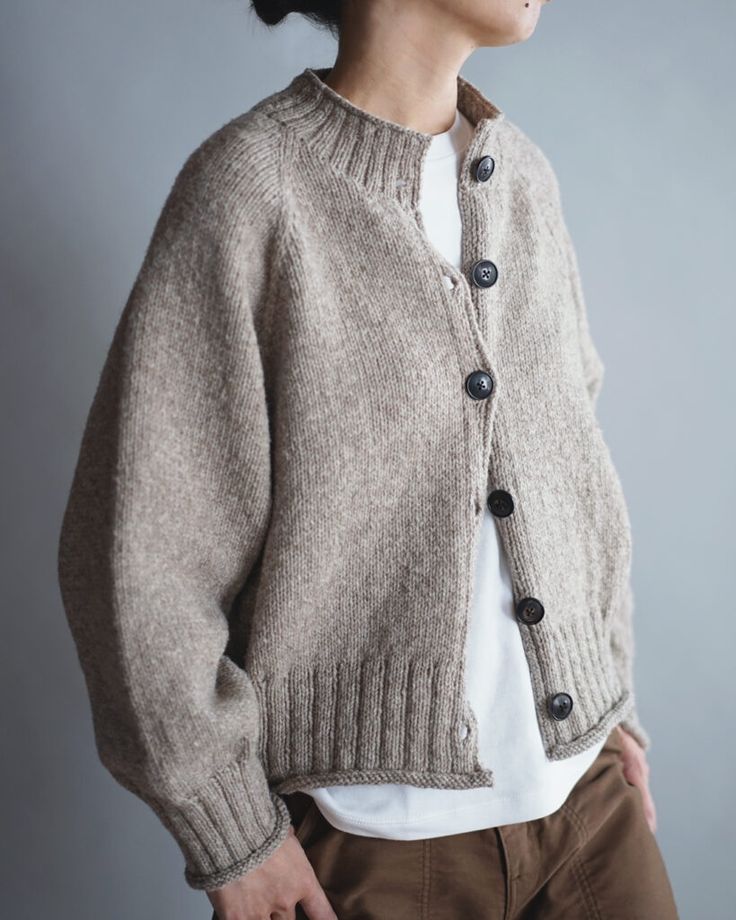 a woman wearing a cardigan with buttons on the front and back, standing against a gray background