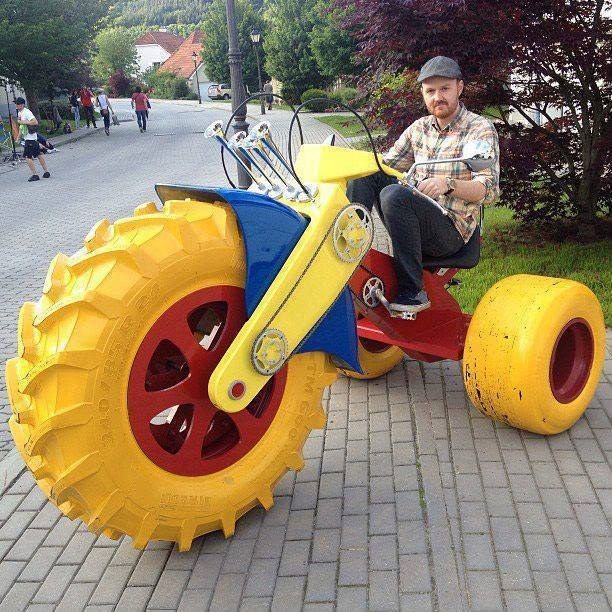 a man sitting on top of a yellow and red toy bike with wheels that are attached to it