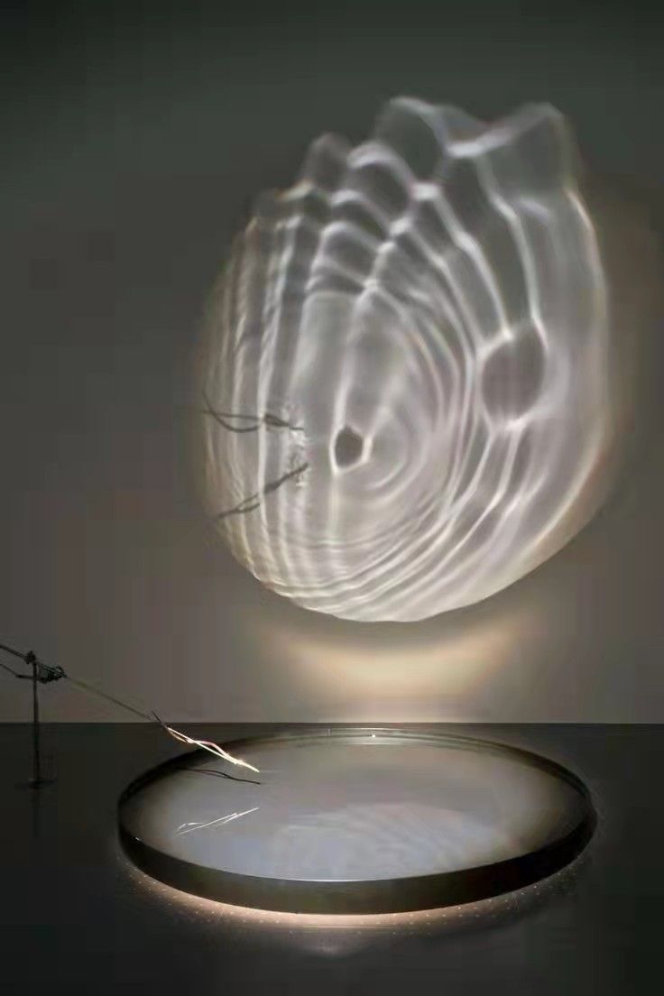 an abstract sculpture is shown in front of a circular light fixture on a black surface