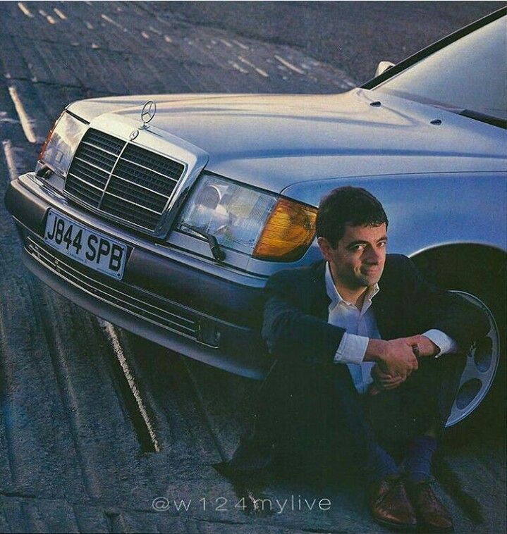 a man sitting on the ground next to a parked car