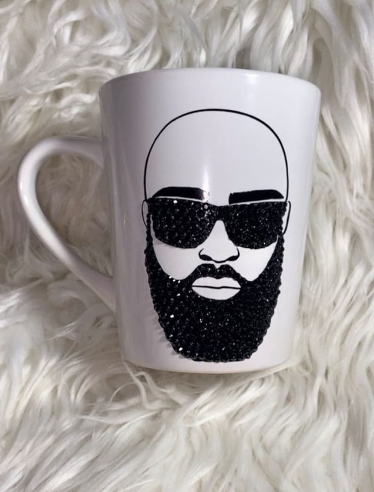 a white coffee mug with a black beard and sunglasses on it's side, sitting on a fluffy surface