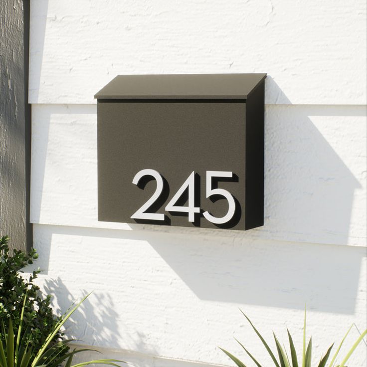 a house number sign mounted to the side of a white building with plants in front of it