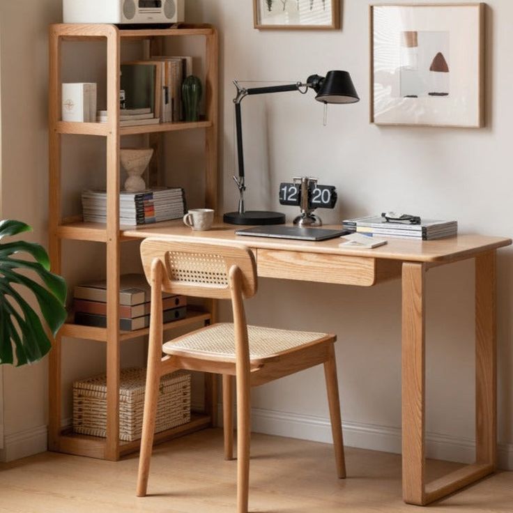 a wooden desk with a lamp, bookshelf and pictures on the wall behind it