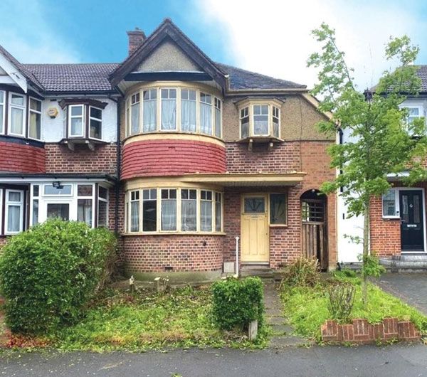 this is an image of a three story house with bushes in the foreground and trees on either side