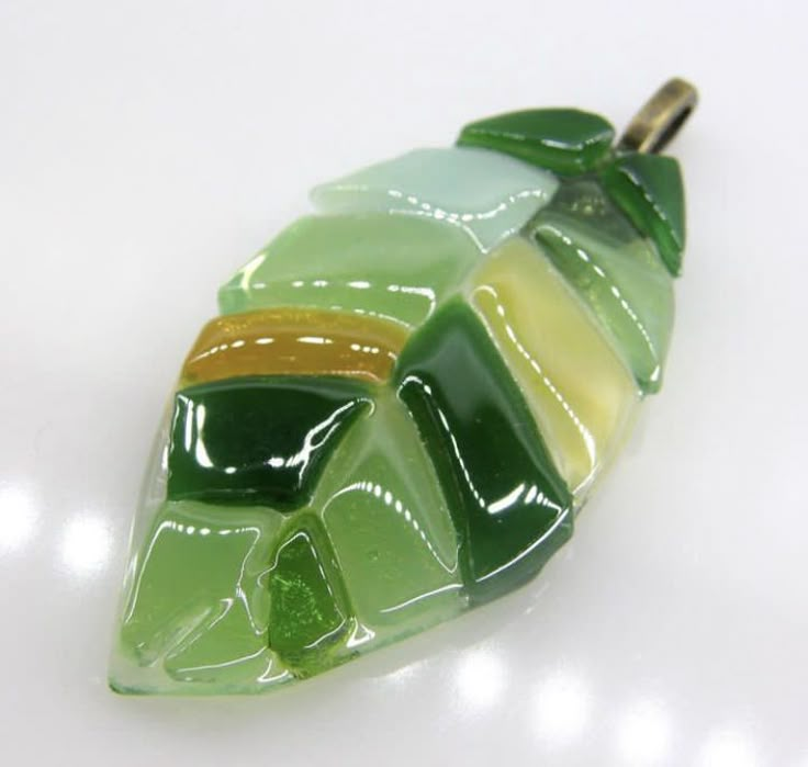 a green and yellow leaf shaped glass object on a white surface with light reflecting off it's side