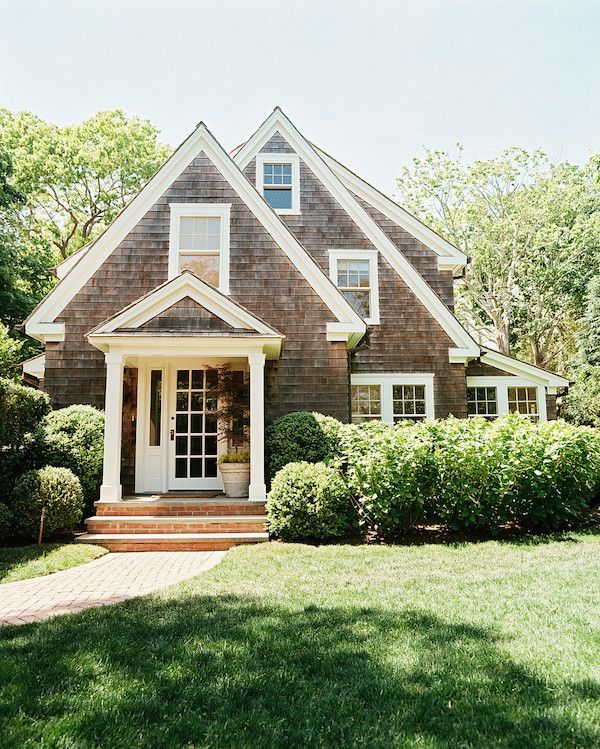 a house that is in the middle of some grass and bushes with trees around it