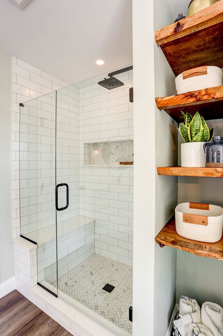 As the focal point of the room, a  freestanding bathtub sits below a large window providing natural light. With the large double vanity, makeup vanity, and exposed shelves, there is no shortage of storage. The beautiful tile shower boasts a tile accent design on the floor and in the niche, and a convenient bench is enclosed in a sleek glass shower door. Shiplap walls, matte black fixtures, and wooden accents are small touches that really bring it all together. Shower With Side Storage, Glass Shower In Small Bathroom, Shower No Tub Ideas Bathroom, Bathroom With No Bathtub, Bathroom Shower With Shelves, Walk In Shower With Storage, Bathroom Decor With Glass Shower Doors, Shower With Bench And Shelves, Shower With Side Shelves