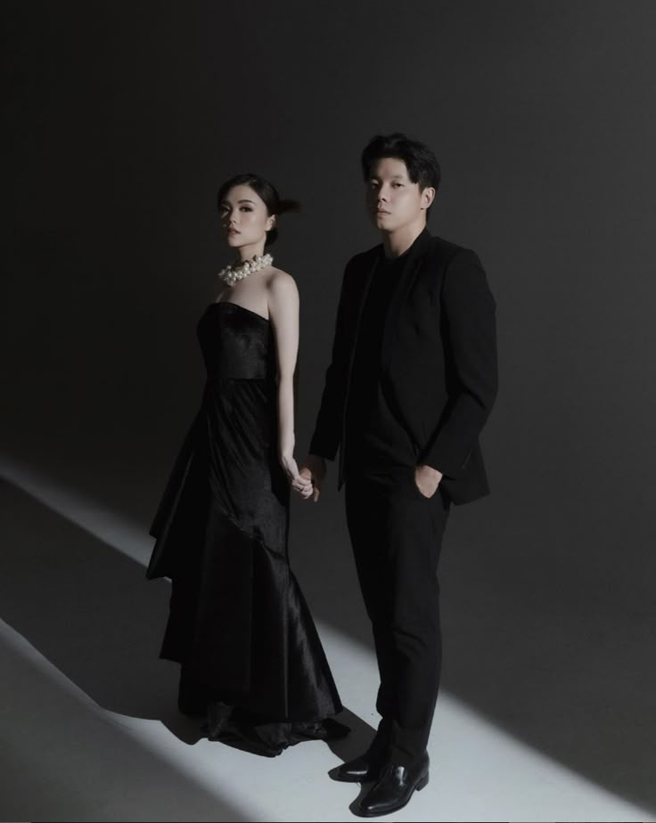 a man and woman standing next to each other in front of a dark background wearing black clothing