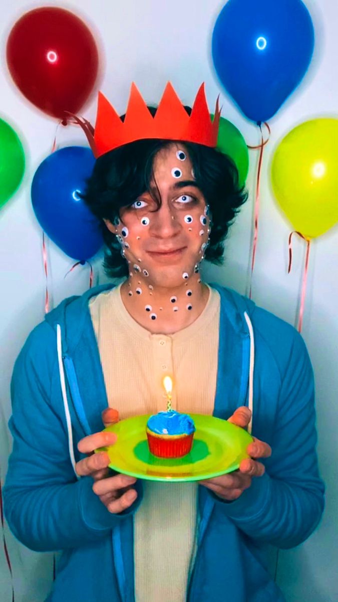 a man holding a plate with a cupcake on it in front of balloons and confetti