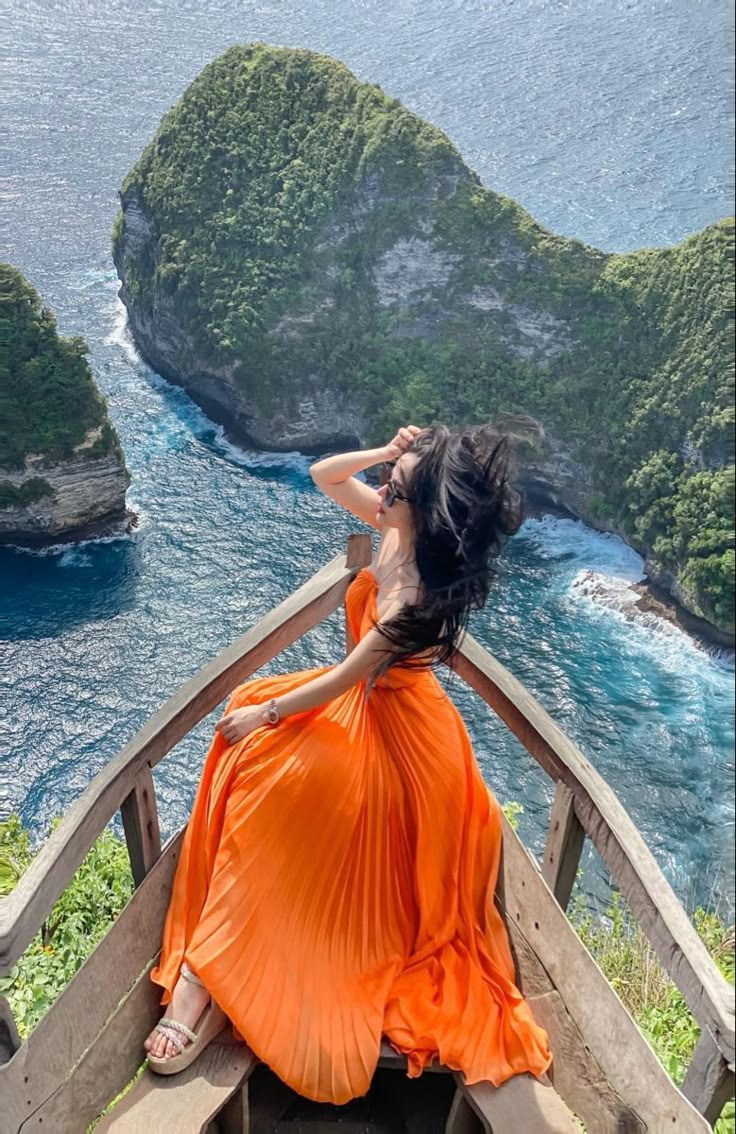 a woman in an orange dress looking out over the ocean