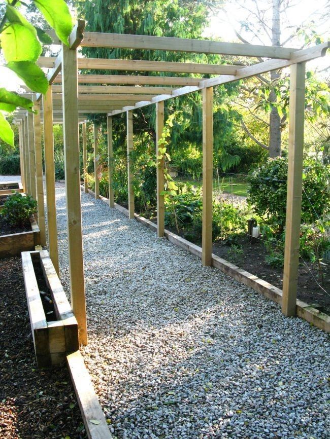 a wooden pergoline in the middle of a garden area with gravel and rocks