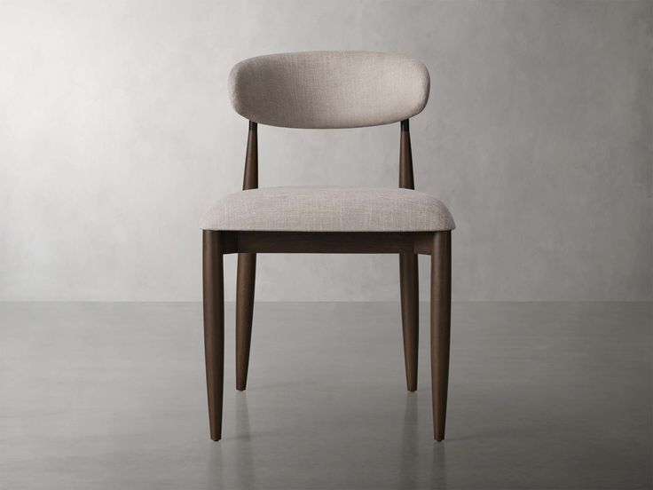 an upholstered chair sits in front of a plain wall and concrete flooring