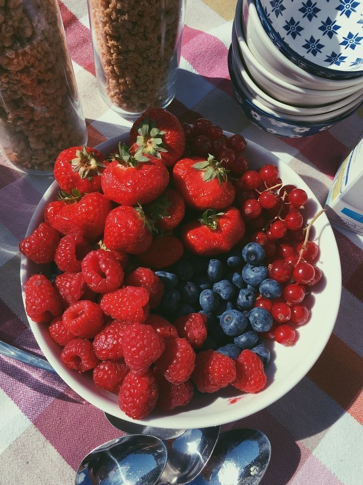 a plate full of berries and blueberries on a checkered table cloth with spoons