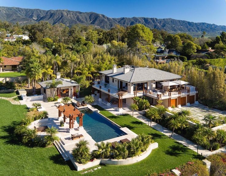 an aerial view of a large home surrounded by trees and mountains with a pool in the foreground