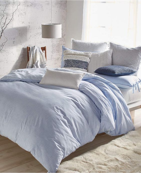 a bed with blue comforters and pillows in a white room next to a window