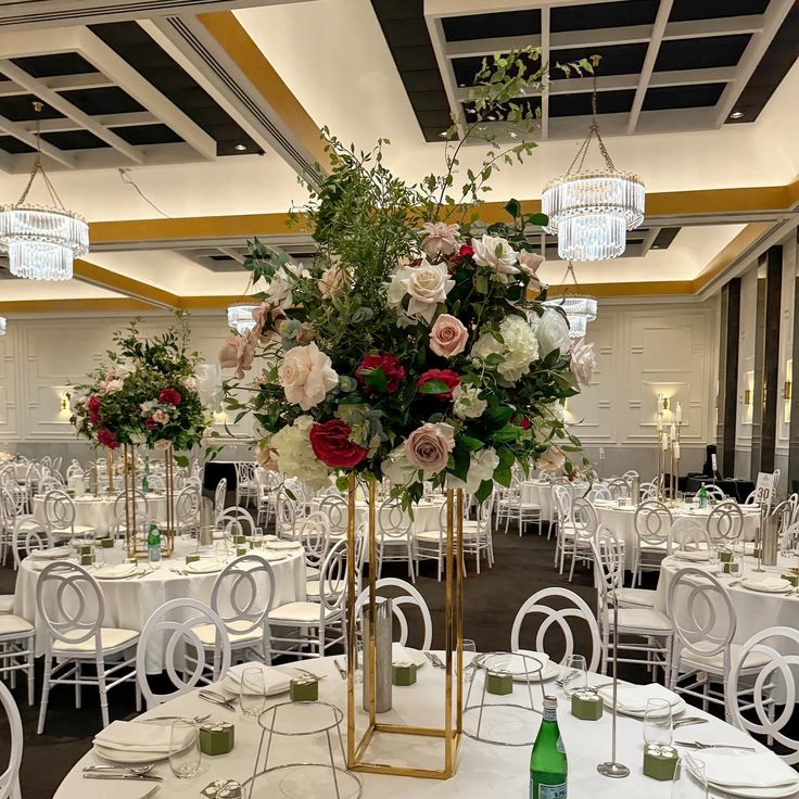 a room filled with tables and chairs covered in white tablecloths, flowers and greenery