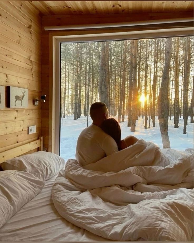 a man and woman cuddle in bed with the sun shining through the trees outside