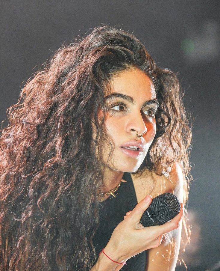 a woman with long hair holding a microphone in front of her face and looking off to the side