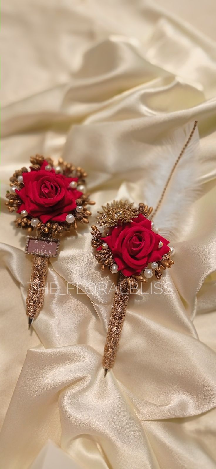 two brooches with red roses on them sitting on a white satin fabric background