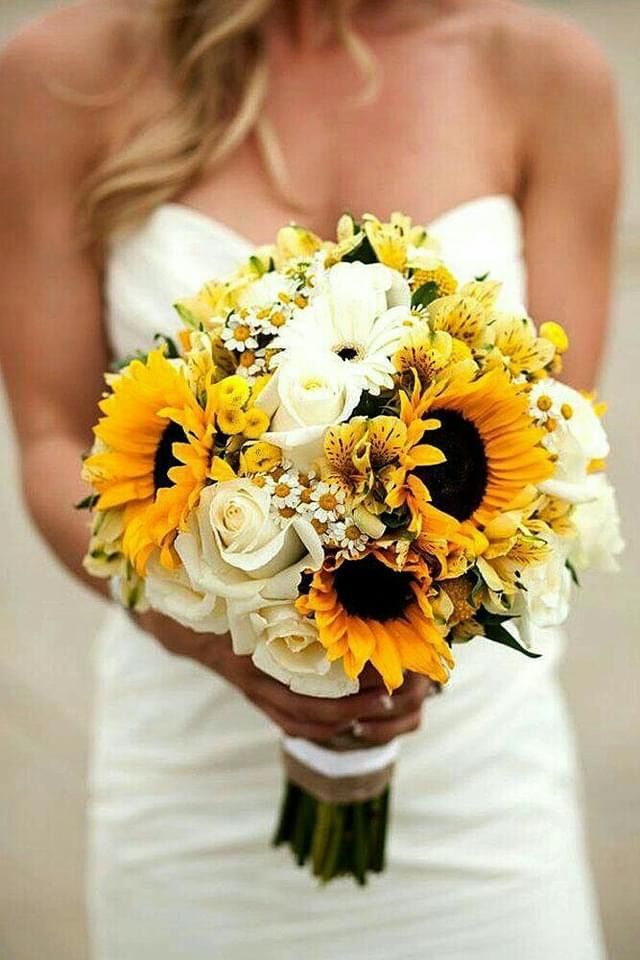 a bride holding a bouquet of sunflowers and other flowers on her wedding day