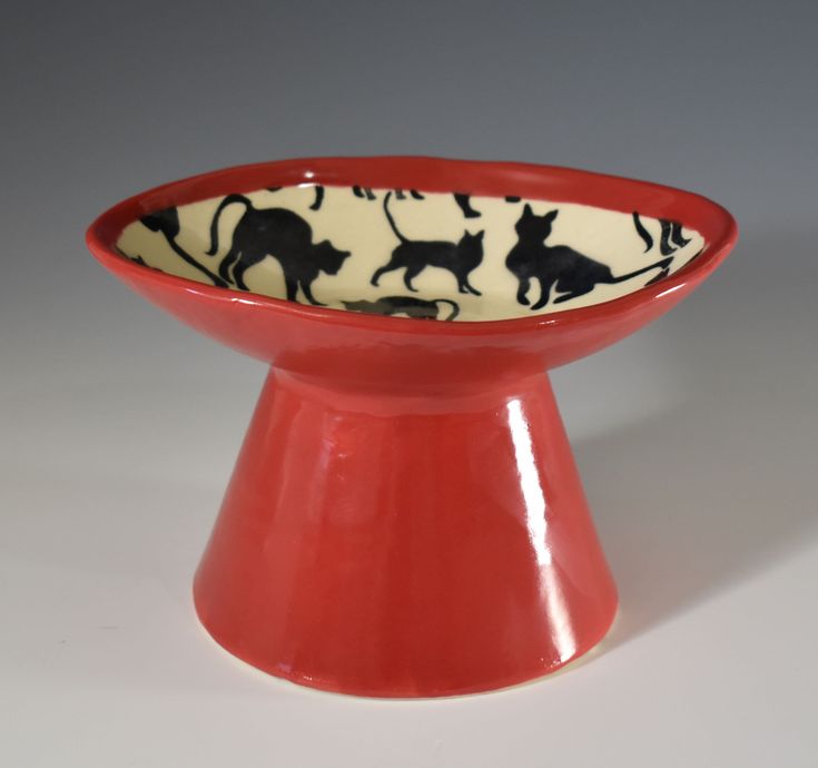 a small red bowl with black cats on it's rim and bottom, sitting in front of a white background