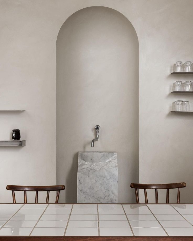 two chairs and a table in a room with white tile flooring on the walls