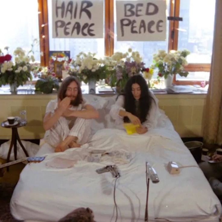 two women sitting on a bed with flowers in the window sill and signs reading hair peace