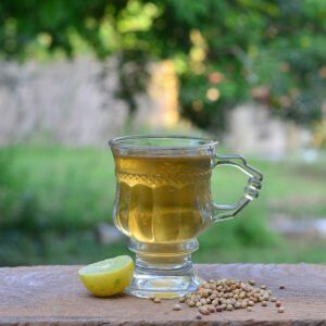 a glass cup filled with tea next to a lemon slice and seeds on a wooden table