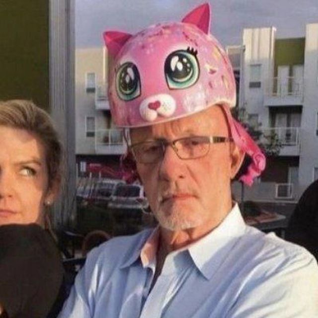 an older man wearing a pink cat hat next to a woman in a white shirt