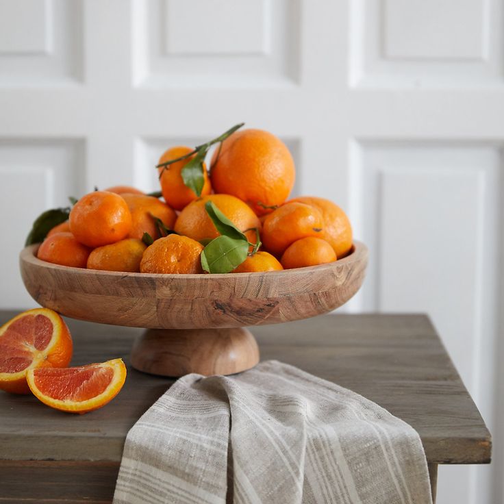 a wooden bowl filled with oranges on top of a table